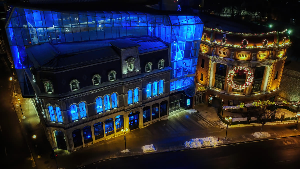 Le Capitole de Québec illuminé de bleu et d'or, vu du ciel à la nuit tombée