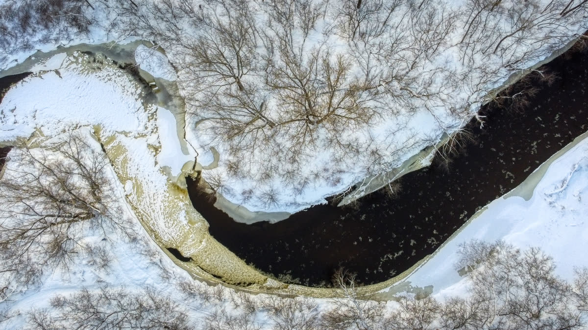 La rivière Duberger gelée, serpentant entre la neige et les arbres nus, vue à la verticale